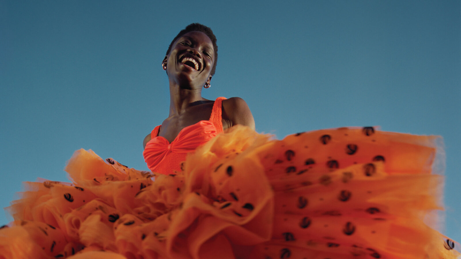 Black model smiling wearing orange tulle dress