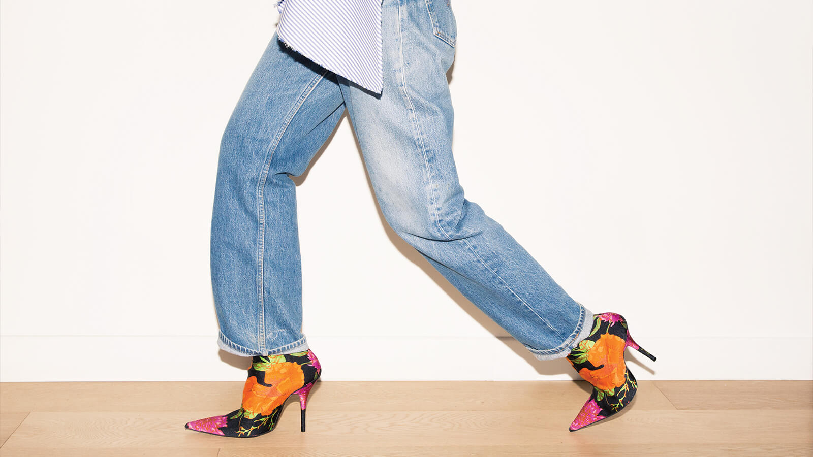 Image of person walking, wearing denim jeans and floral heeled boots