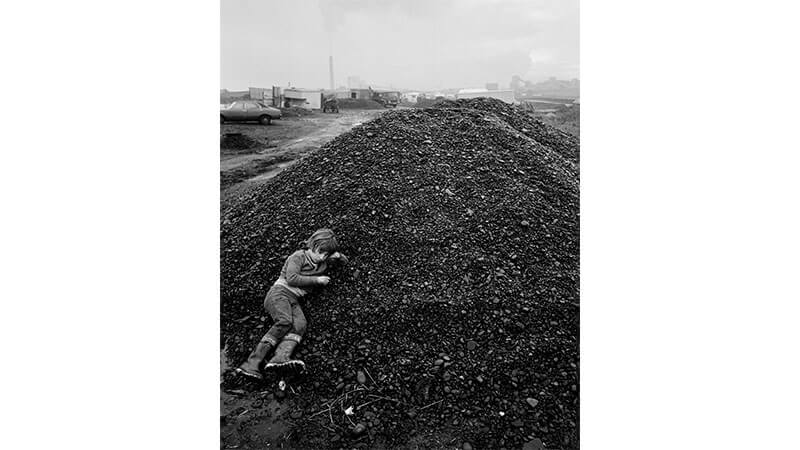Black and white archive image of a young boy lying on a pile of coal in Lynemouth, Northumberland