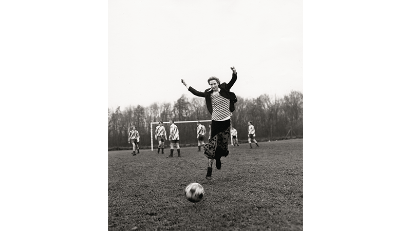 Black and white photo girl playing football in skirt