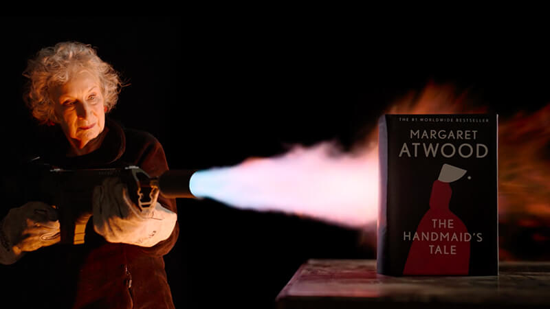 Image of author Margaret Atwood burning Handmaid's Tale book with flame