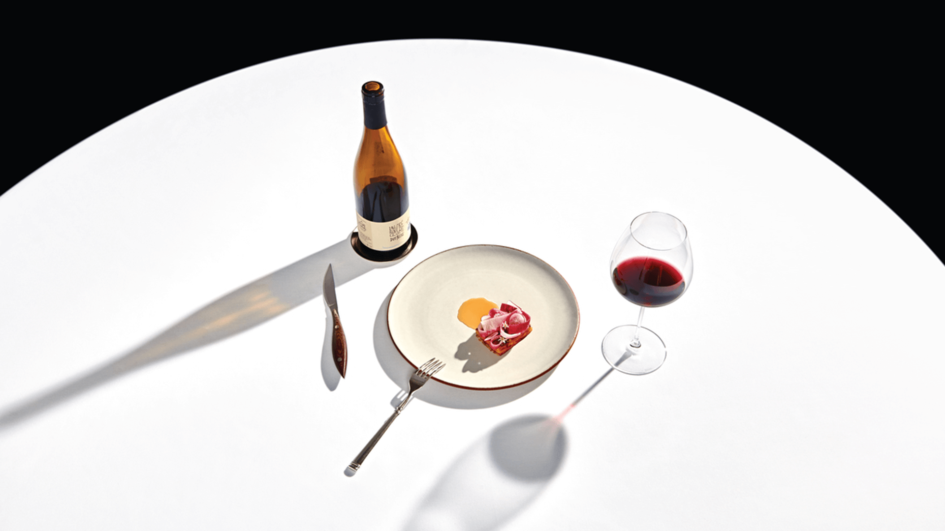 White table with bottle of red wine and single dish